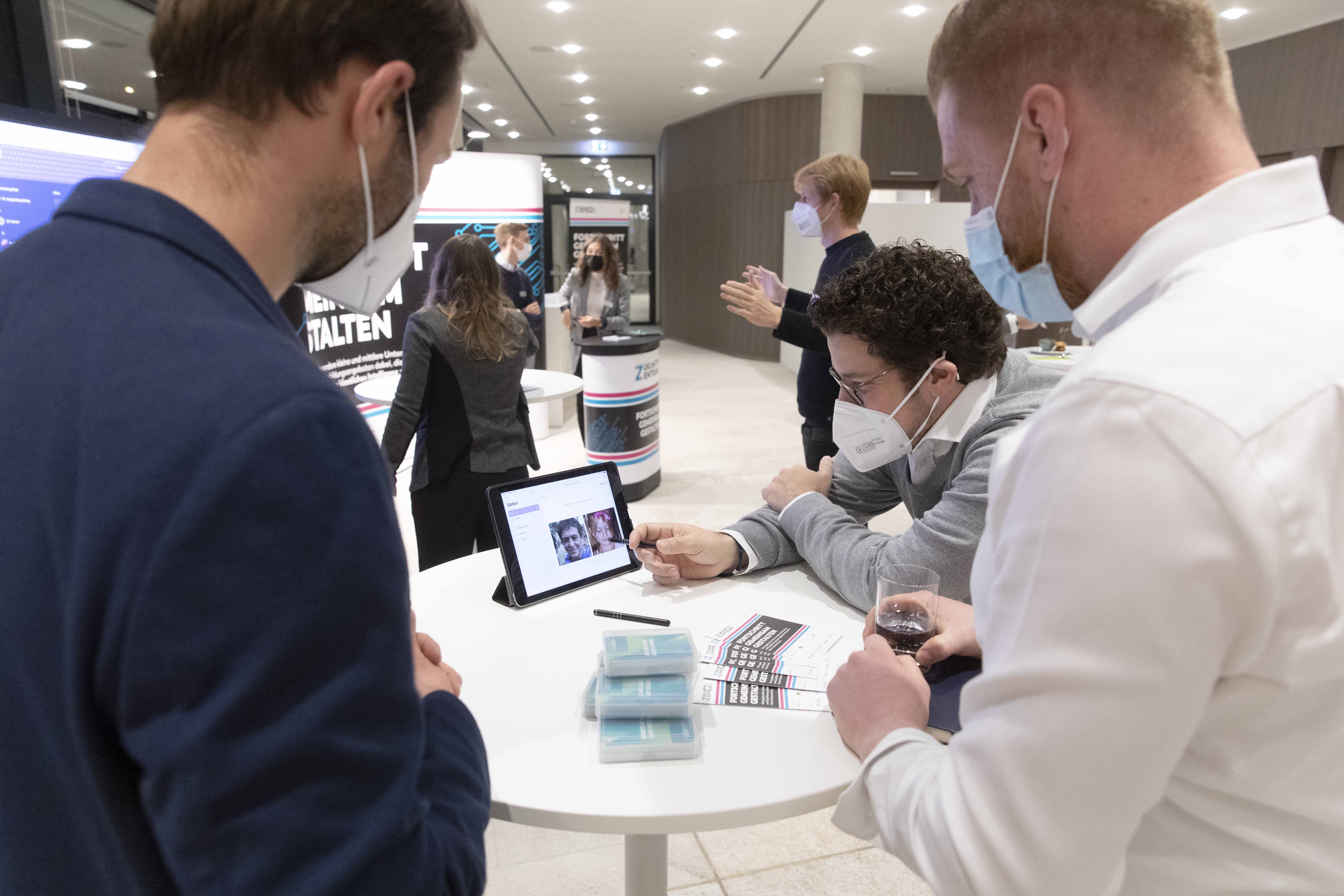 Drei Personen mit medizinischen Masken testen Software an einem Tablet